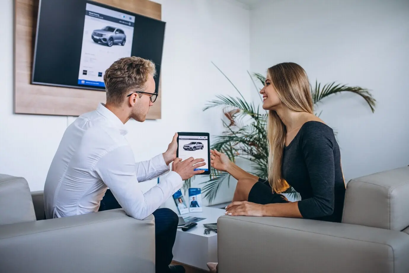A man and a woman use a tablet in a car showroom.